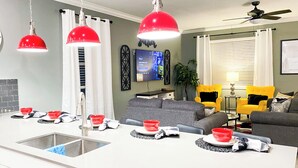 A modern kitchen with a central island, a dining area with a sofa and chairs, and a living room with a TV and decorative items.