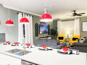 A modern kitchen with a central island, a dining area with a sofa and chairs, and a living room with a TV and decorative items.