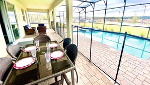 A covered patio with a glass table set for dining, overlooking a swimming pool.