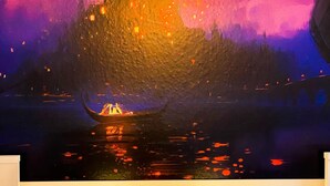 A room with a large wall mural of a castle and a boat, two table lamps with sun designs, and a white table.