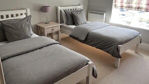 Une chambre avec deux lits, une table de chevet, une lampe et une fenêtre donnant sur la rue.