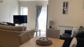 Un salon comprenant un canapé, un téléviseur, une table à manger avec des chaises et une fenêtre avec des rideaux.