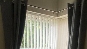 Une pièce dotée d’une grande fenêtre recouverte de stores blancs et de rideaux gris, ainsi que d’un sol recouvert d’une moquette.