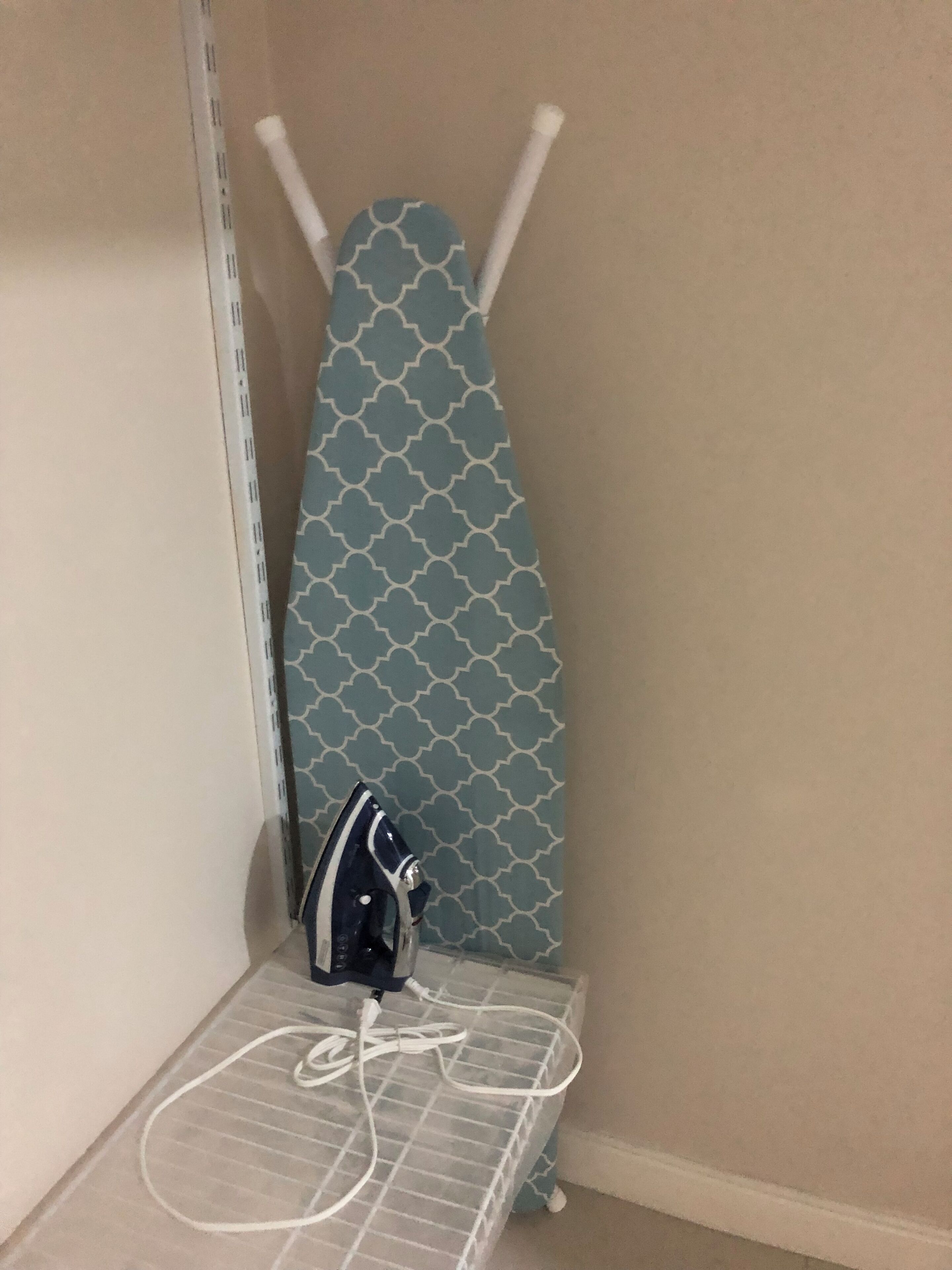 A corner of a room with a patterned ironing board, an iron, and a power strip.