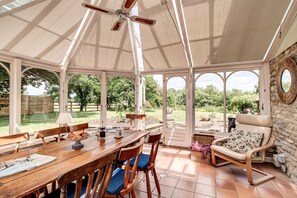 Une véranda avec une table en bois, des chaises et un fauteuil rembourré.