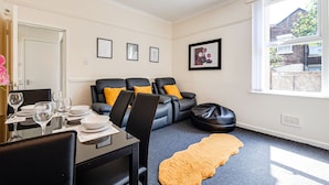 Un salon moderne avec un coin repas, comprenant un ensemble de canapés, une table à manger avec des chaises et une grande fenêtre donnant sur l’extérieur.