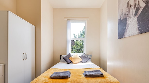 Une chambre d’hôtel étroite, avec un lit, une fenêtre et une armoire.