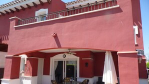 Ein rotes Gebäude mit einem Balkon, einer überdachten Terrasse mit Tisch und Stühlen sowie einer Tür mit Fenster.