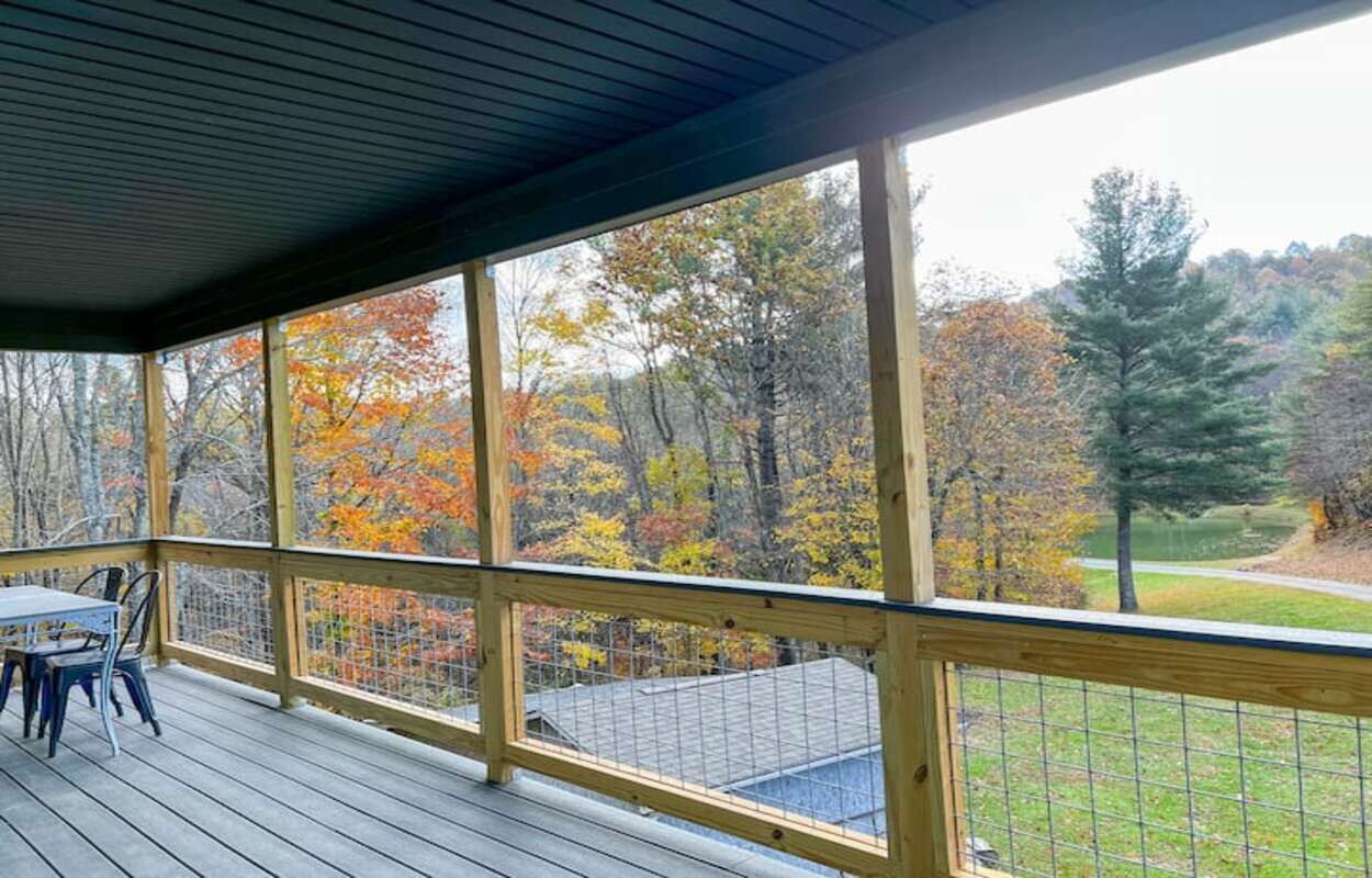 Eine überdachte Terrasse mit Blick auf Herbstbäume und eine Rasenfläche.