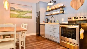 A modern kitchen with stainless steel appliances, wooden cabinets, and a dining area with a wooden table and chairs. - Heartwood♥ Cabin loft w/private HotTub, Hiking, Fishing, & Ziplines on 66 acres! (Floyd)