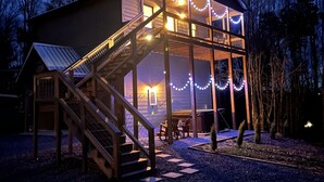 A wooden cabin with a covered porch, a staircase, and string lights. - Heartwood♥ Cabin loft w/private HotTub, Hiking, Fishing, & Ziplines on 66 acres! (Floyd)