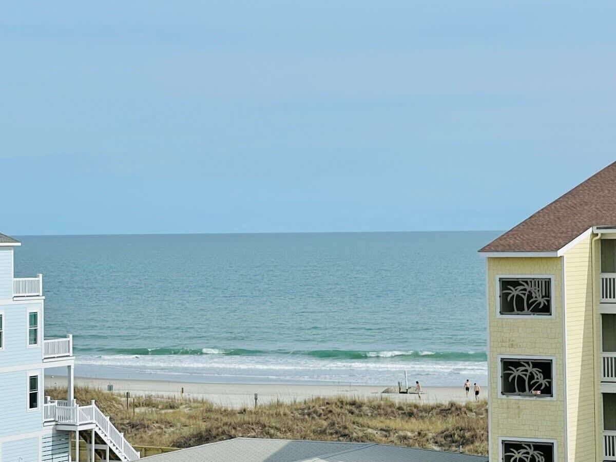 Une propriété située en bord de mer, offrant une vue sur l’océan, la plage et un immeuble doté d’un balcon.