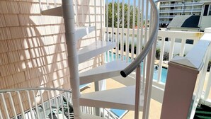 Eine Wendeltreppe mit weißen Geländern und Blick auf einen Pool sowie Gebäude im Hintergrund.