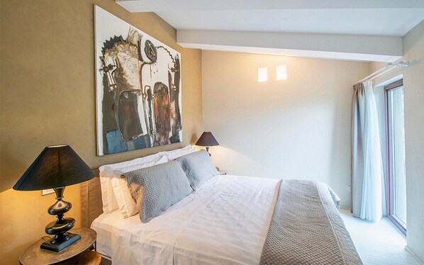 A hotel room with a large bed, two bedside lamps, a painting on the wall, and a window with curtains.