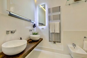 A modern bathroom with two large white sinks, a wooden vanity, a towel rack, a mirror, and a bidet.