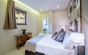 A bedroom with a bed, a bedside table with a bowl, a mirror, and a painting on the wall.