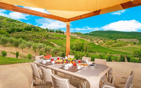 An outdoor dining area with a table set for breakfast, overlooking a vineyard.