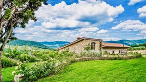 A rustic stone house with a tiled roof, surrounded by lush green fields and mountains in the background. - VILLA CHIANTI ROSSO - Four Bedroom Villa, Sleeps 9 (Greve in Chianti)