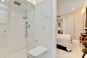 Un baño moderno con cabina de ducha de vidrio, un inodoro y una cama en la habitación contigua.