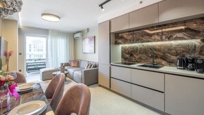 A modern kitchen with a marble backsplash, a dining area with a table set for two, and a living area with a sofa and a coffee machine. - Apartment Val di Sole II (Porec)