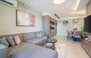 A modern living room with a grey sectional sofa, a small round coffee table, and a dining area with a table and chairs. - Apartment Val di Sole II (Porec)