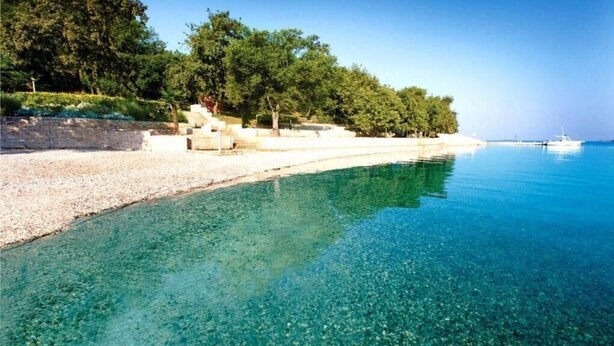 A clear, shallow beach with a pebble shore and a calm sea. - Apartment Val di Sole II (Porec)