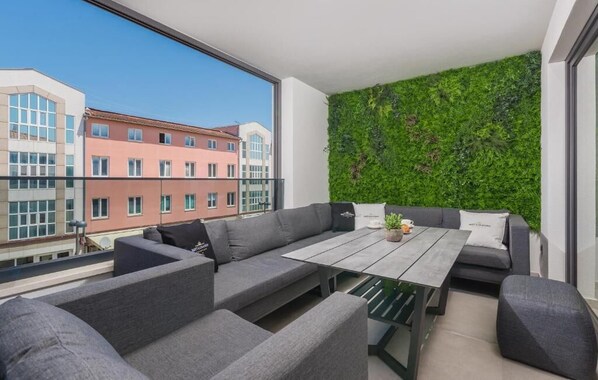 Un balcón moderno con un sofá gris, una mesa de madera y un muro vertical con jardín.
