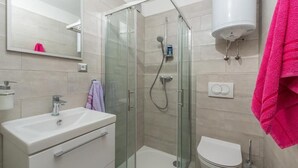 Un baño moderno con ducha envuelta en vidrio, lavamanos blanco y un inodoro.