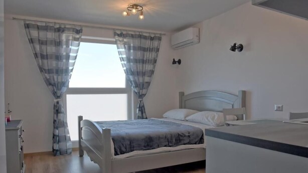 Un dormitorio con cama, cómoda, ventana con cortinas y una lámpara en el techo.