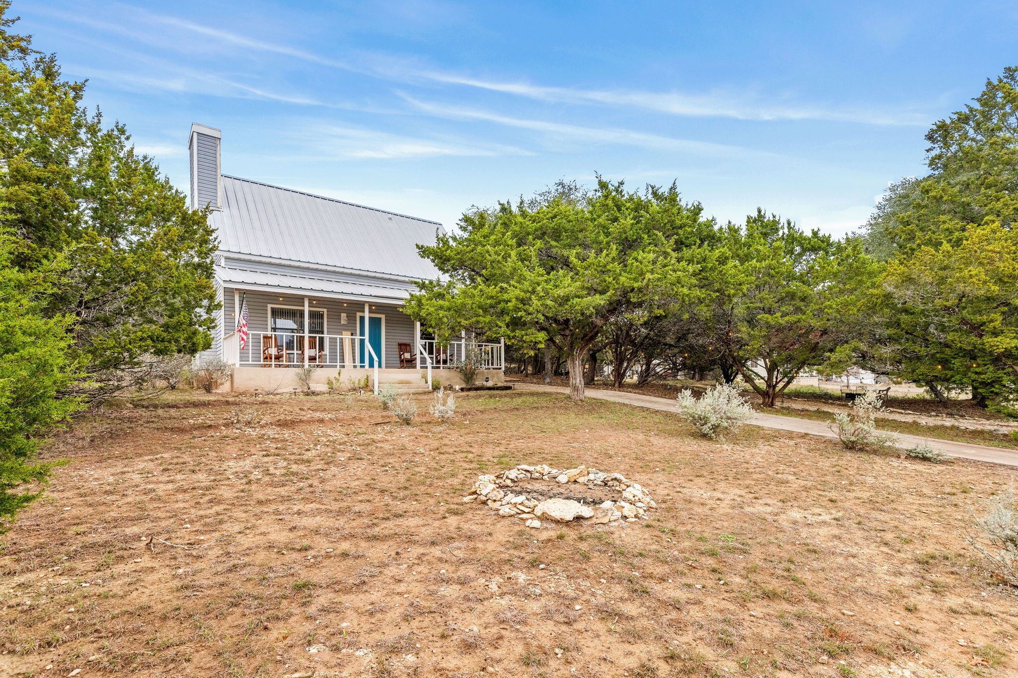 A single-story house with a covered porch, surrounded by trees and a dry grassy yard.