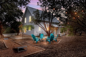 A house with a fire pit and chairs in the backyard, surrounded by trees and a gravel area. - Blue Door Cottage Family Game Room - Family Friendly! (Canyon Lake)