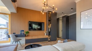 Un salon moderne avec un canapé, une table basse et un téléviseur fixé à un mur en bois. On y trouve également un fauteuil et une petite table sur laquelle est posée une plante.