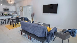 Una sala de estar moderna con un sofá, una mesa de comedor y un televisor montado en la pared.