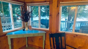 Une pièce au décor intérieur en bois, avec un bureau dont le plateau est bleu, une chaise et de grandes fenêtres donnant sur une terrasse et des arbres.