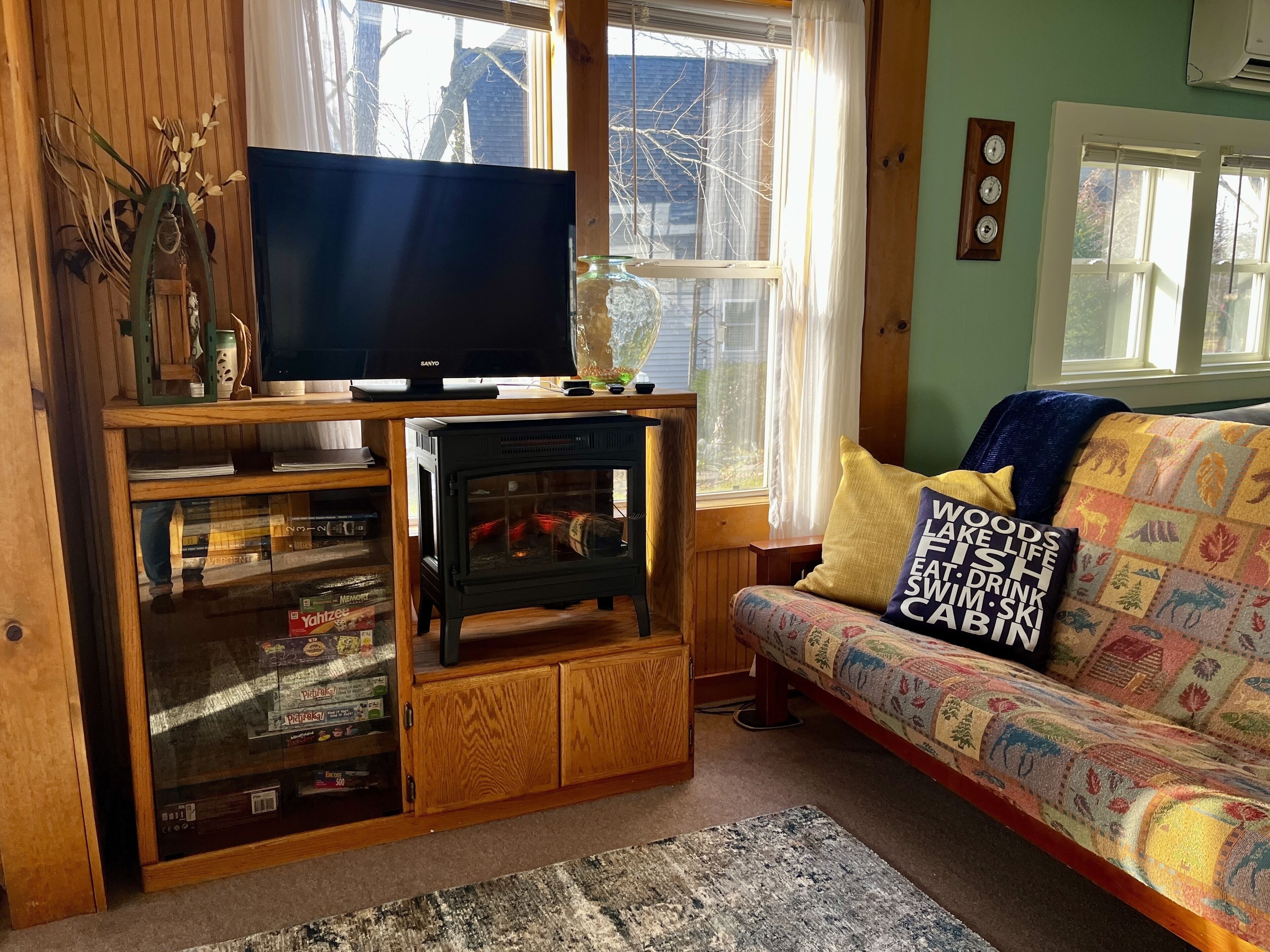 Uma sala de estar aconchegante com televisão sobre um suporte de madeira, lareira, sofá com almofadas coloridas e janela com cortinas.