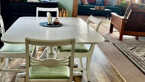 Un coin repas avec une table et des chaises blanches, un plancher en bois et des œuvres d’art encadrées accrochées aux murs.
