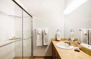 A modern bathroom with a glass shower enclosure, a sink with a mirror, and two towels hanging on the wall.