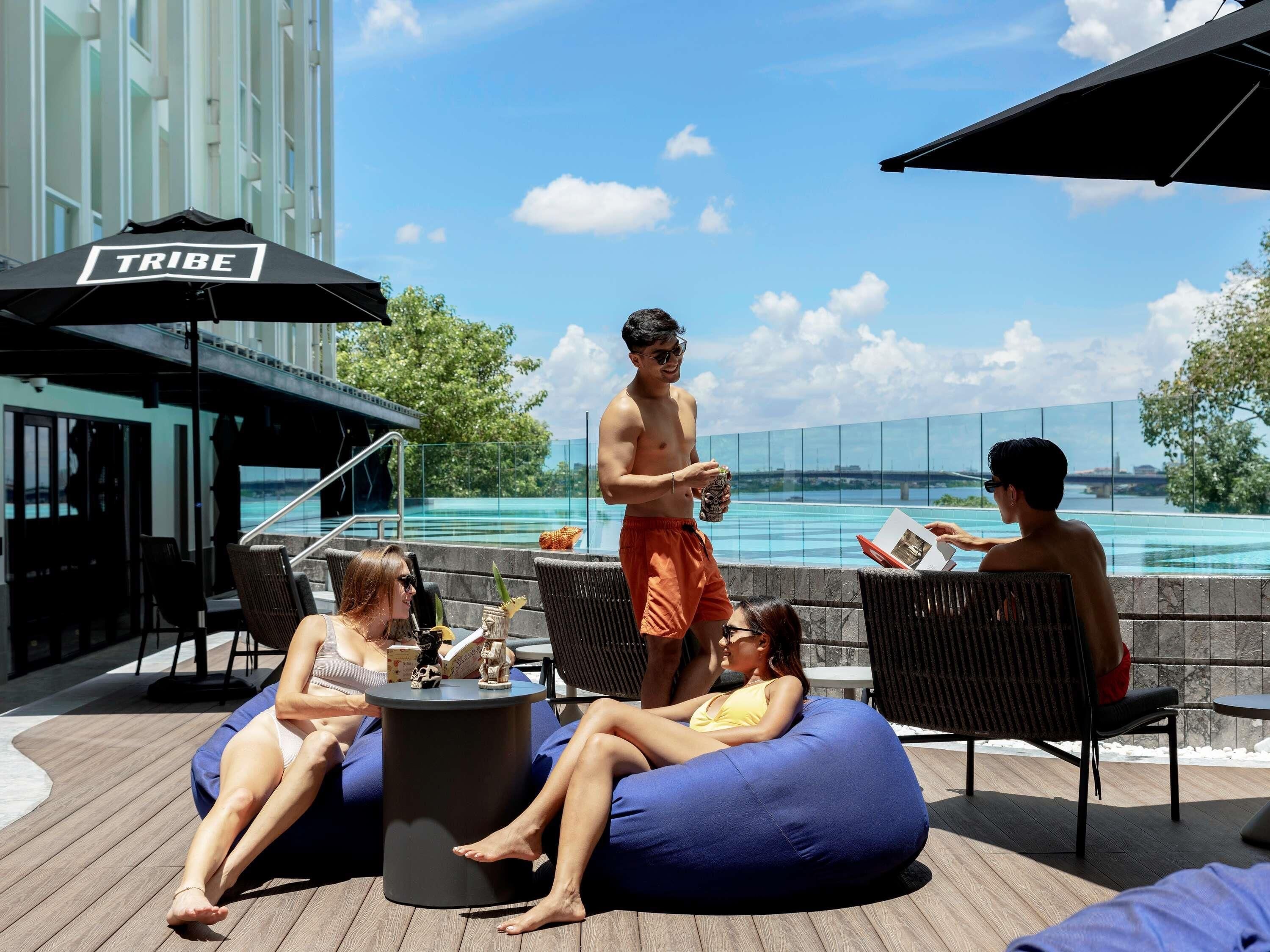 A poolside area with lounge chairs, a table, and a sign labeled 'TRIBE'.
