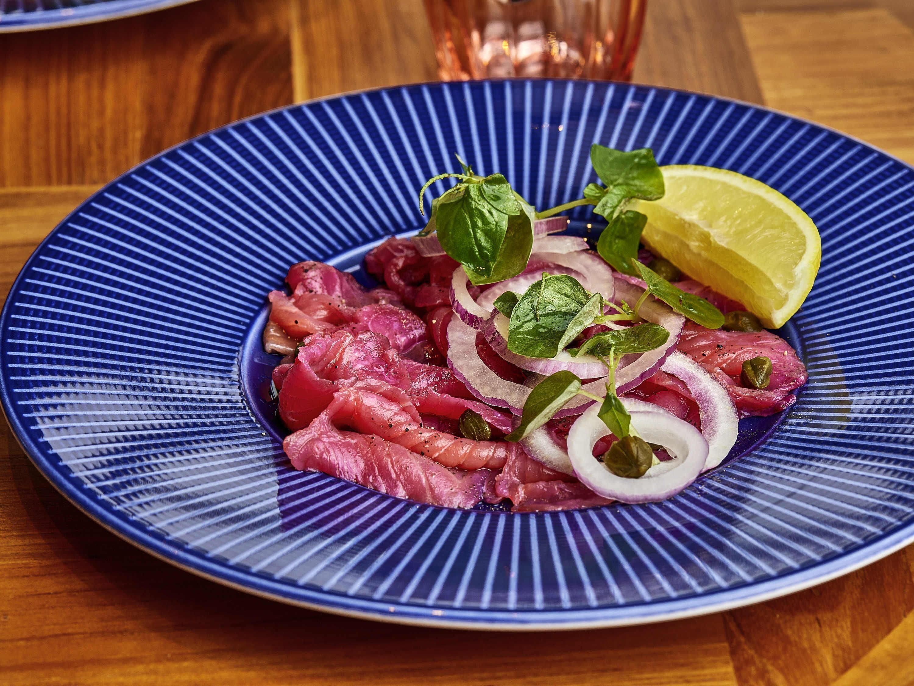 A blue plate with thinly sliced meat, onions, and a lemon wedge.