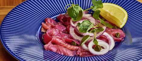 Um prato azul com carne fatiada finamente, cebolas e uma fatia de limão.