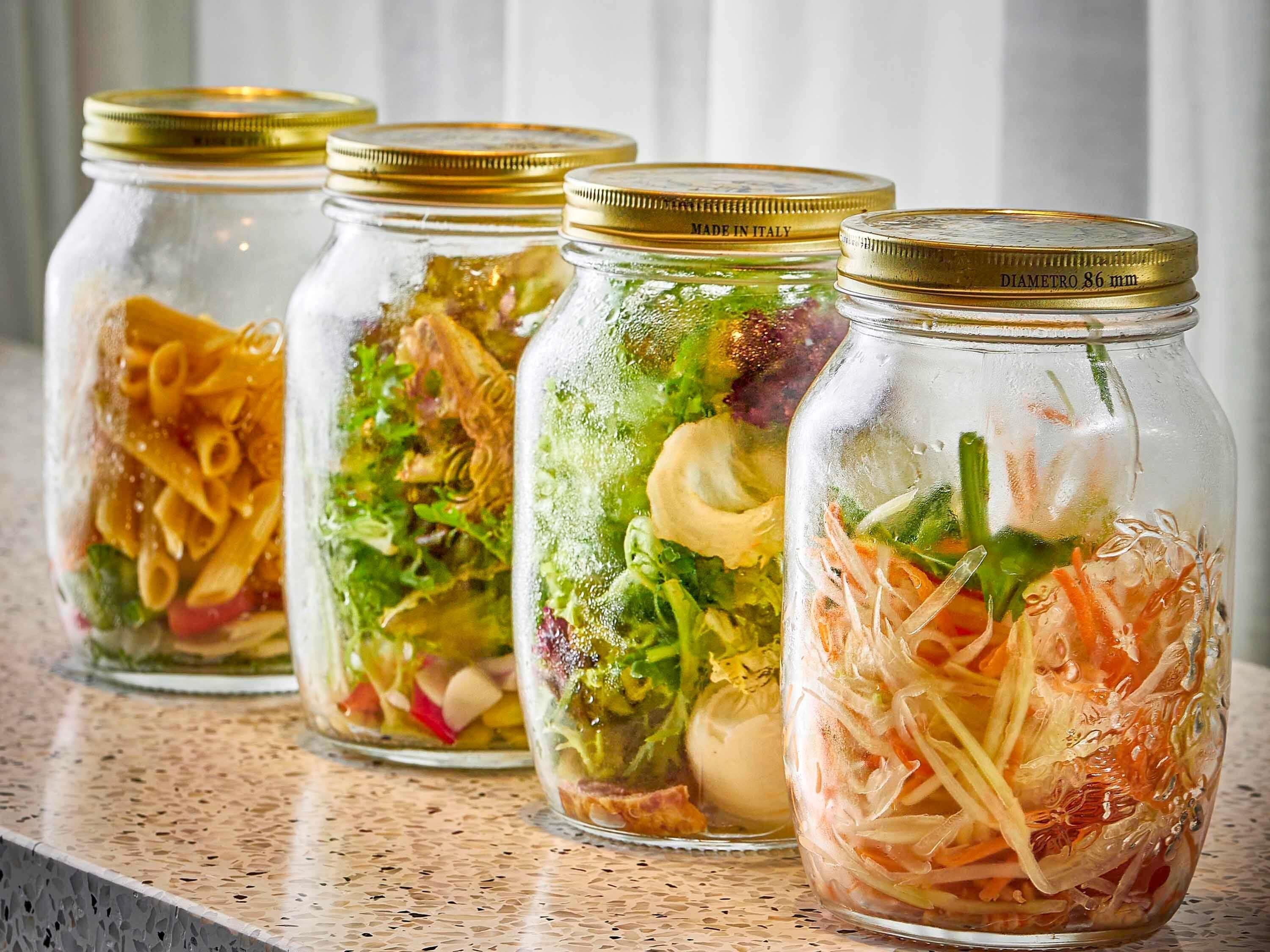 Four glass jars with golden lids containing salads.