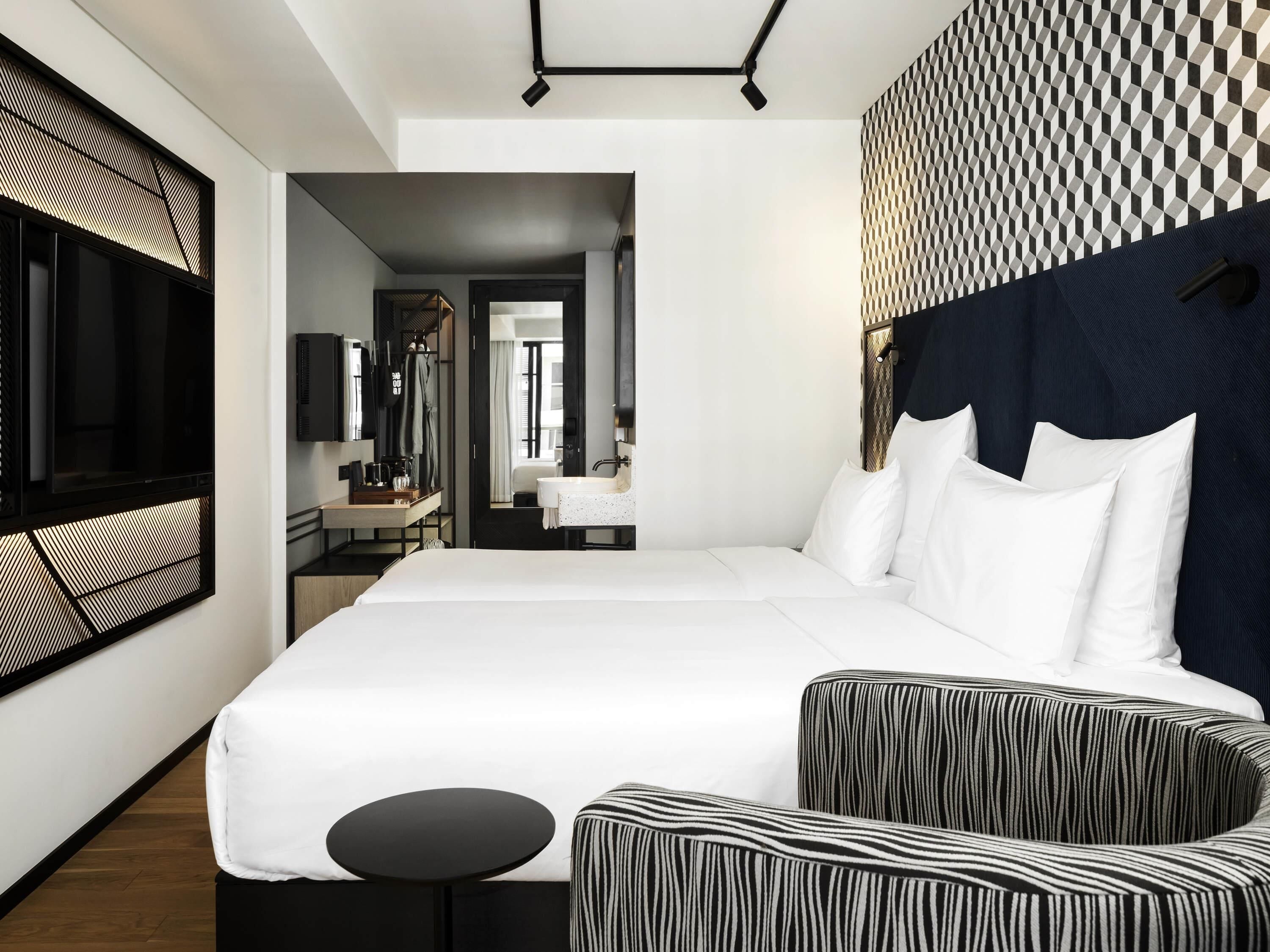 A modern hotel room with a large bed, a small round table, and a seating area with striped cushions.