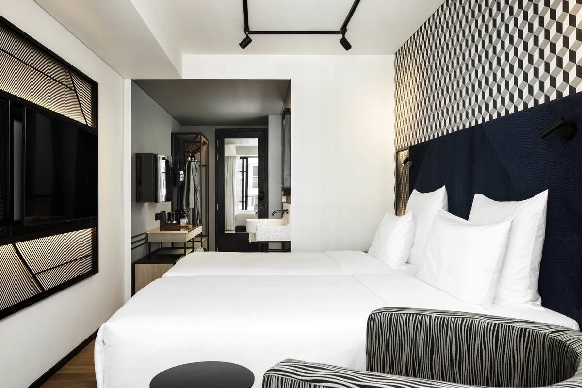 Une chambre d’hôtel moderne avec un grand lit, une petite table ronde et un coin salon agrémenté de coussins à rayures.