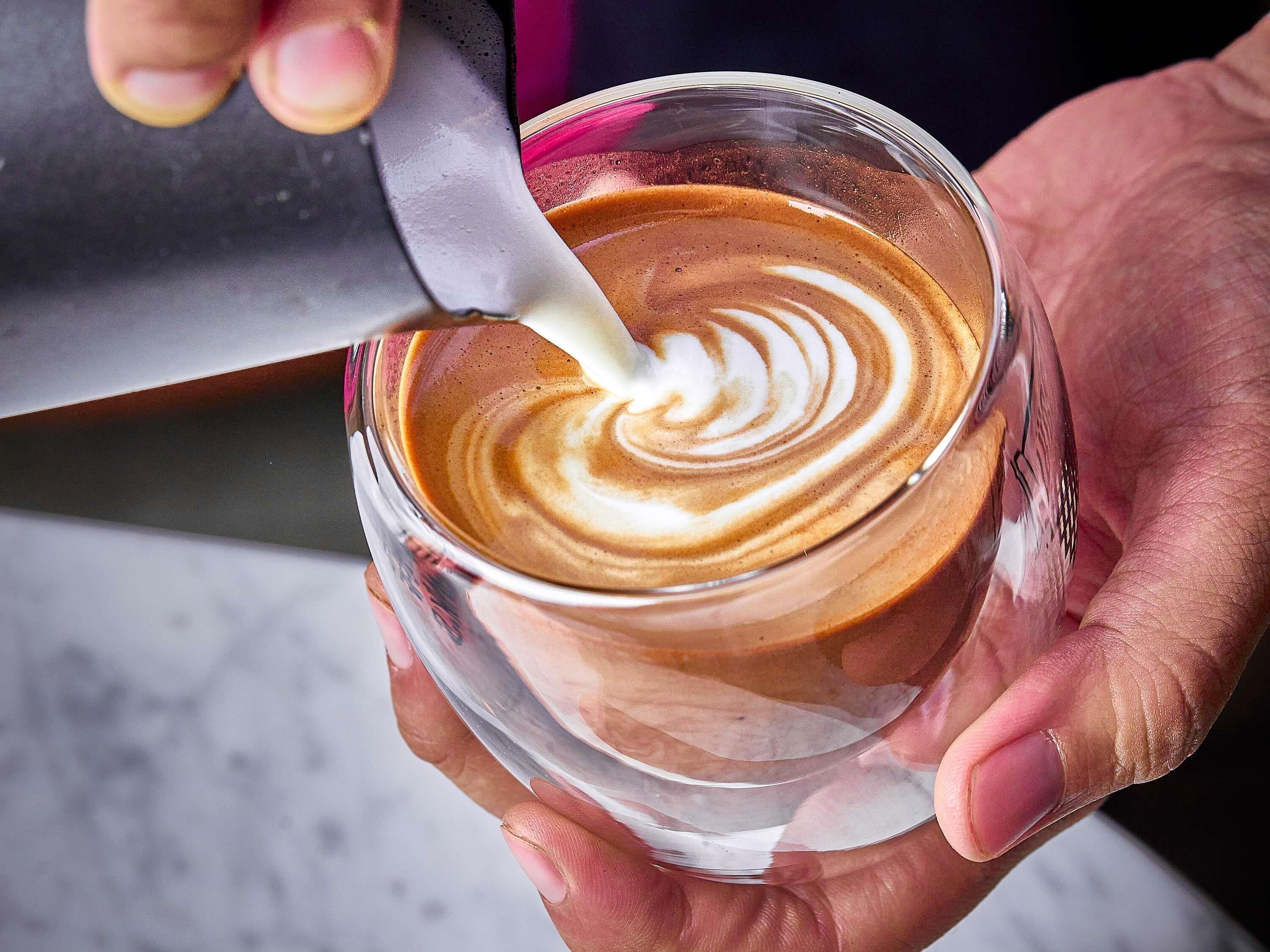 Una persona sosteniendo una taza de café con un dibujo de arte latte.