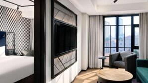 A modern hotel room with a large bed, a round table, a sofa, and a city view through large windows. - TRIBE Phnom Penh Post Office Square (Phnom Penh)