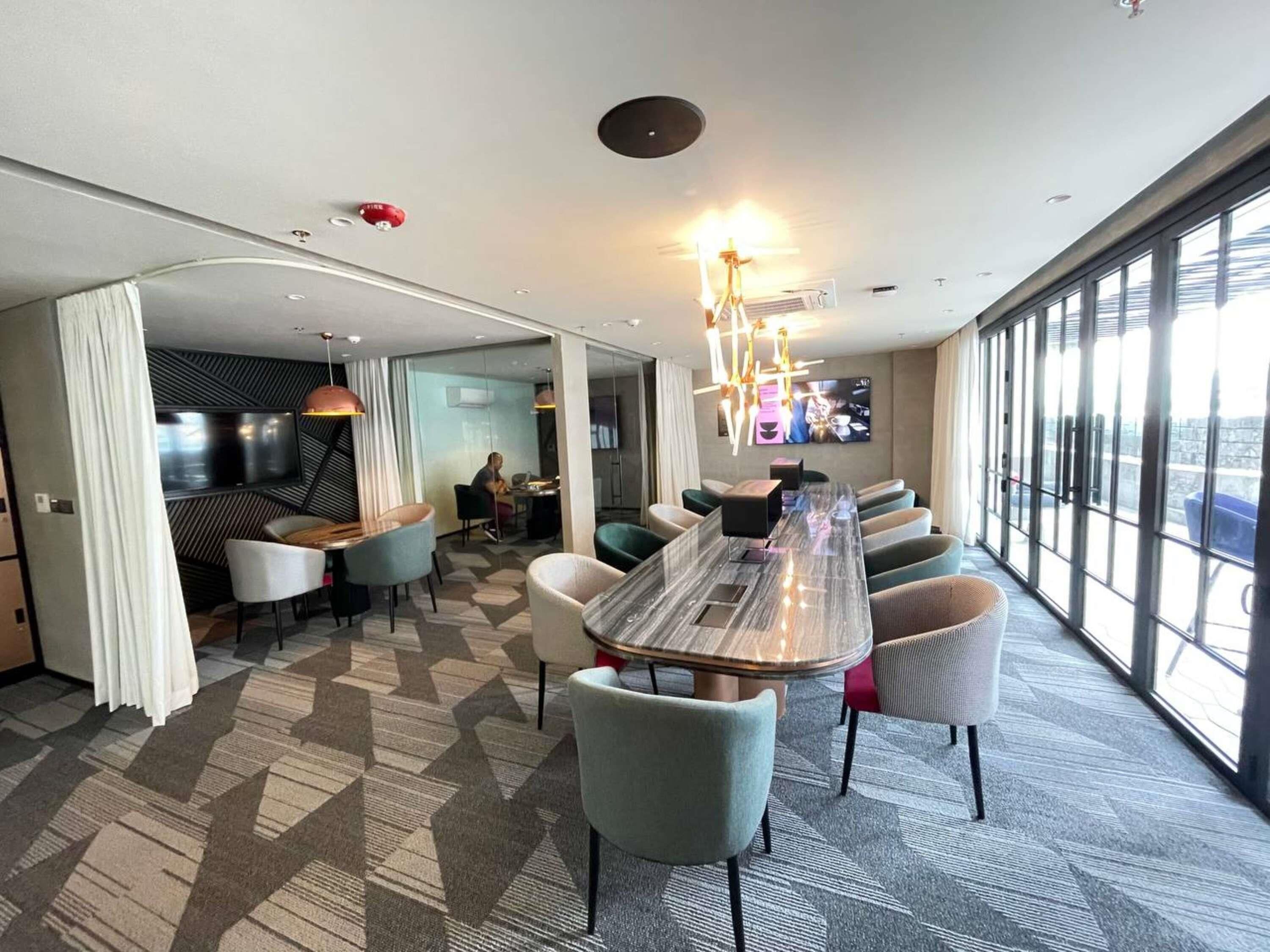 Et moderne hotelværelse med et stort spisebord, behagelige siddepladser, et fjernsyn og store vinduer med udsigt over byen.