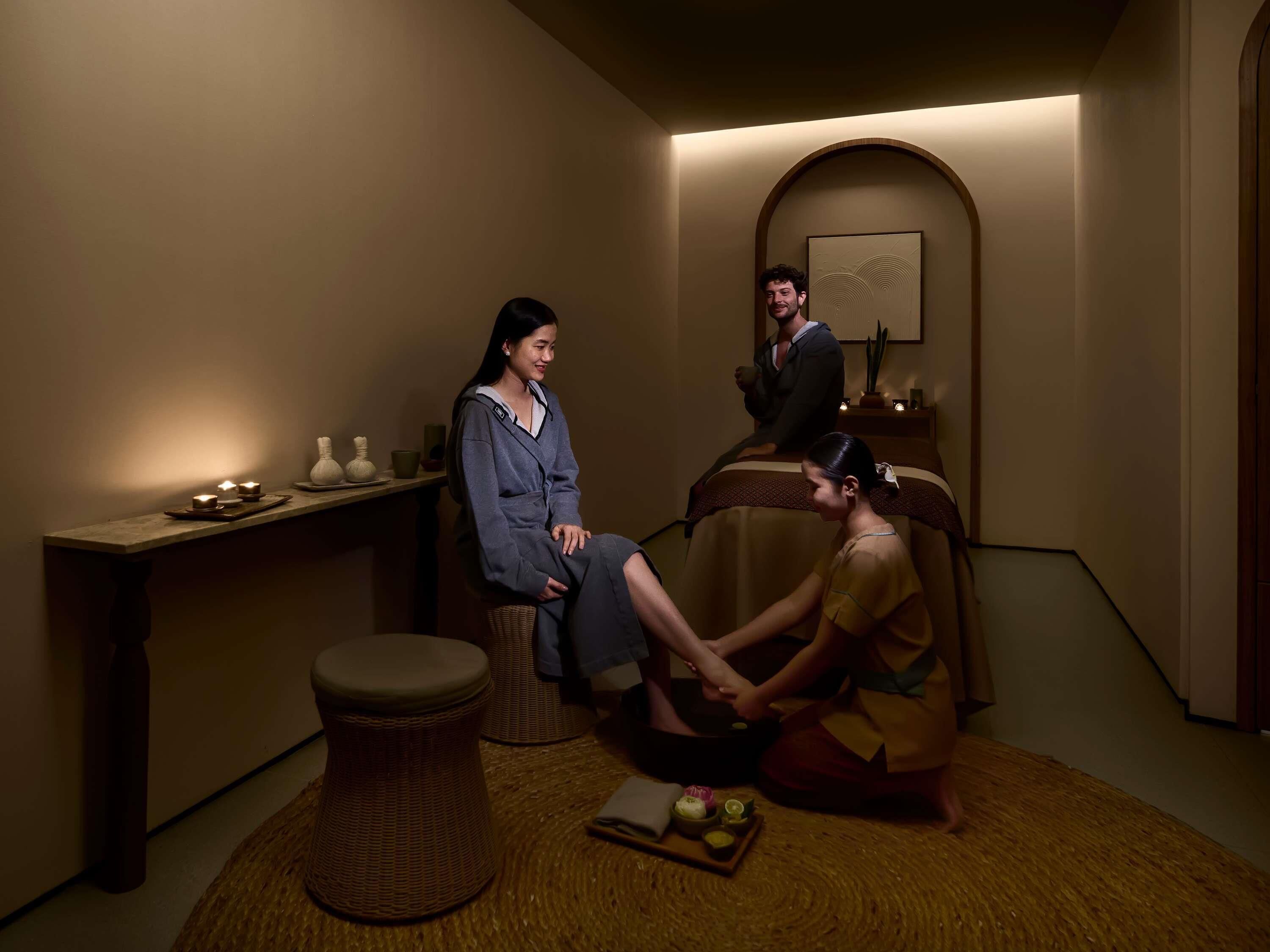 Une pièce avec un lit, une petite table avec des bougies et un tabouret en osier.