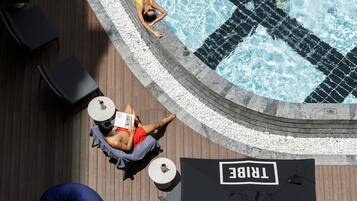 A poolside area with a hot tub, lounge chairs, and a table with a drink.