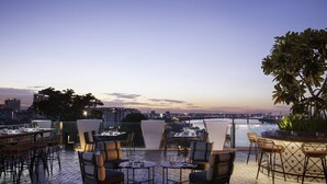 An outdoor seating area with tables and chairs, overlooking a cityscape and a body of water. - TRIBE Phnom Penh Post Office Square (Phnom Penh)