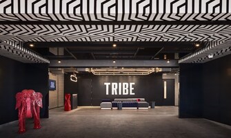 Un interior moderno con un diseño geométrico en el techo, un llamativo letrero 'TRIBE' y muebles contemporáneos.